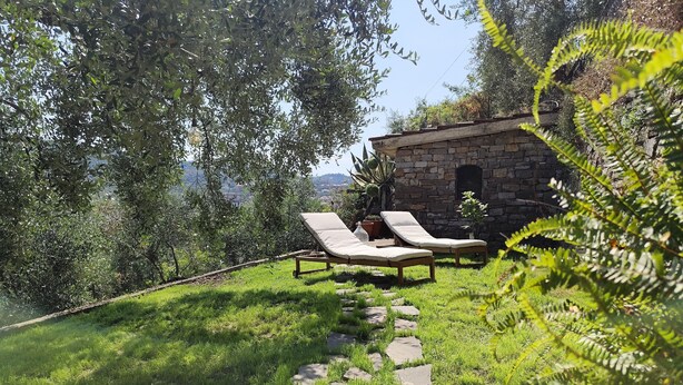 Un edificio de piedra con un camino de piedra que lleva a un área con césped y dos sillones de relax.