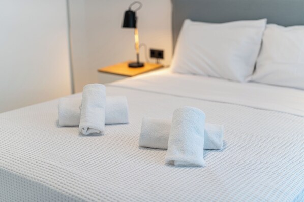 A neatly made bed with white linens and a small bedside table with a lamp. - Emerald Island Residential Complex (Skála Rachoníou)