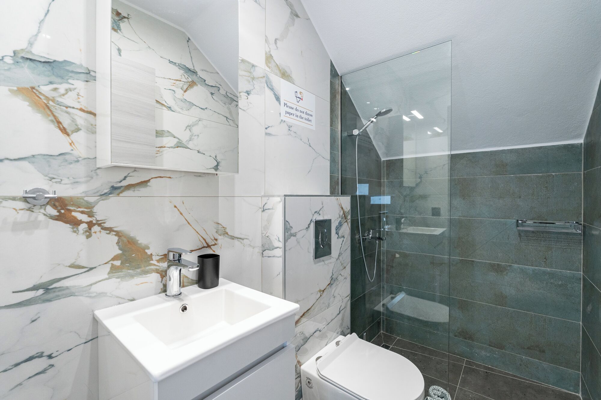 A bathroom with a marble wall, a sink, a toilet, and a glass-enclosed shower.