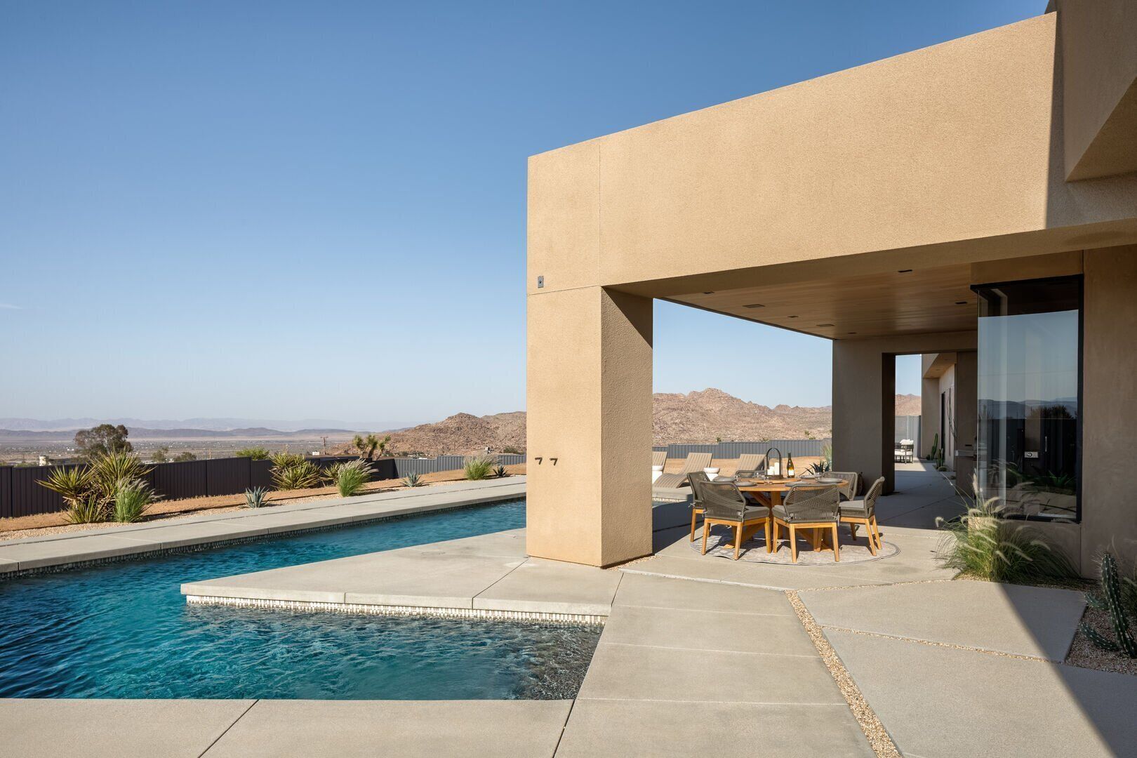A modern house with a swimming pool, outdoor seating, and a view of the desert landscape.