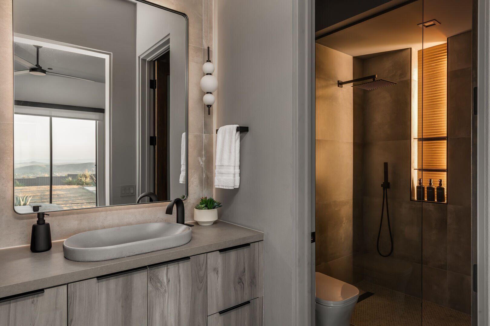 A modern bathroom with a large mirror, a sink, a shower, and a toilet.
