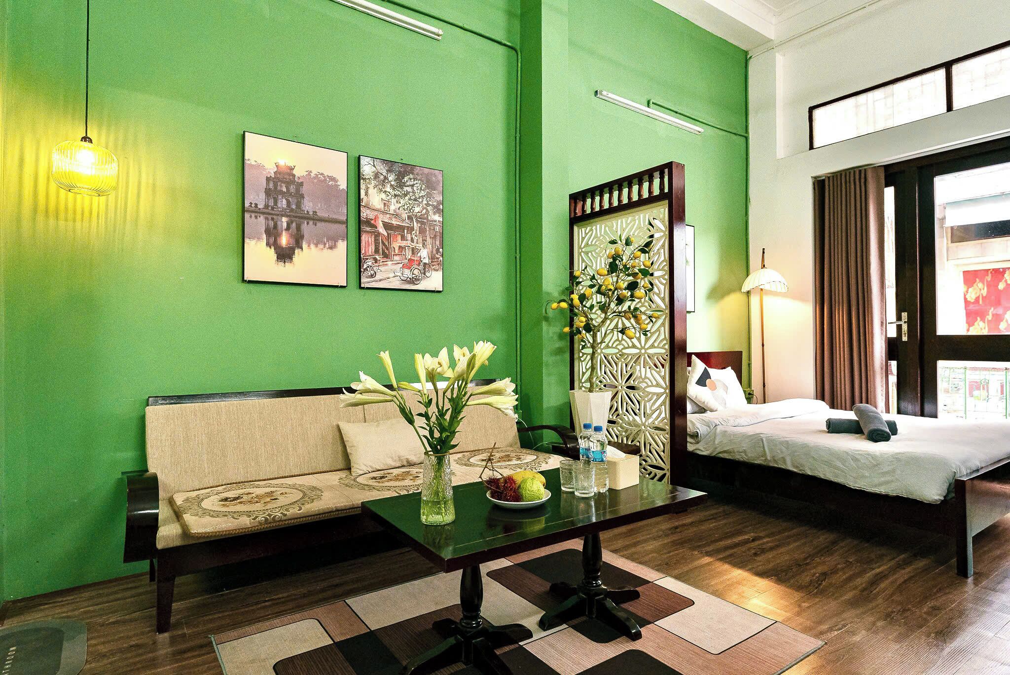 Habitación de hotel con una pared verde, un sofá, una cama, una mesa con un florero y cuadros enmarcados.