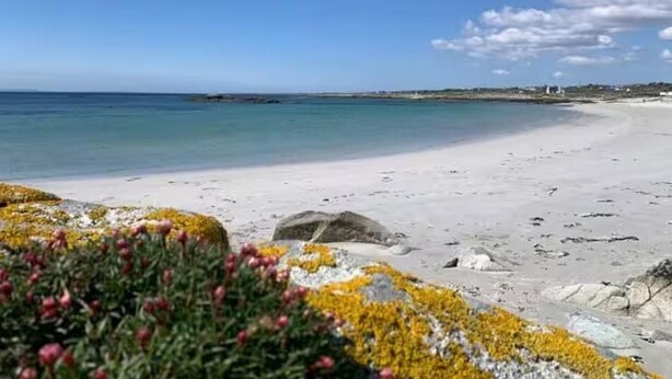 En strand med klart, blått vatten, en sandstrand och några stenar.
