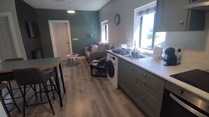 Ett kompakt kök med tvättmaskin, en matplats med stolar, ett litet bord och en soffa.