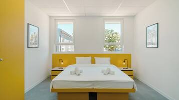 A modern bedroom with a bed, two bedside tables, and two windows.