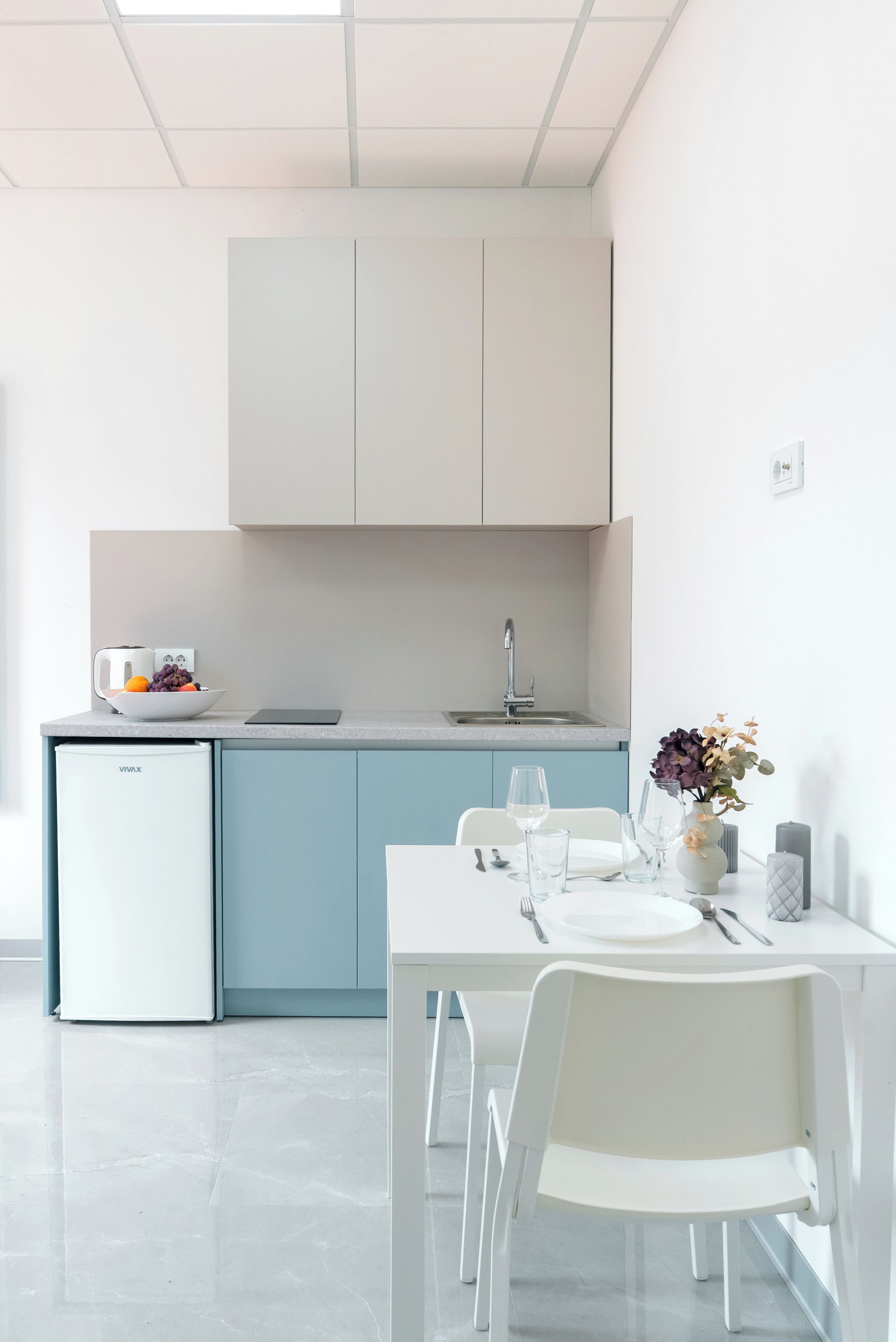 A modern kitchen with a built-in fridge, a dining table with chairs, and a vase with flowers on the table.