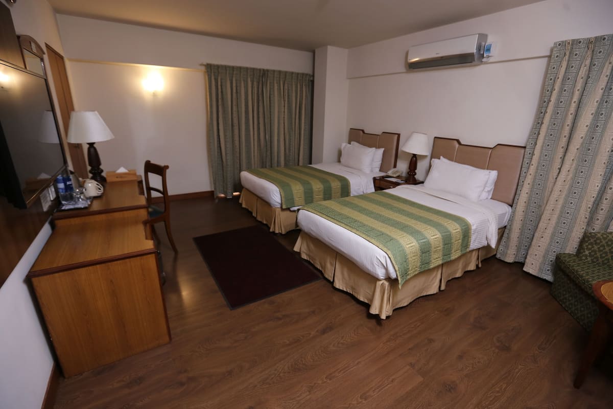 A hotel room with two beds, a desk, a chair, a mirror, and a window with curtains.