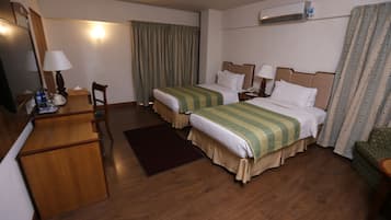 A hotel room with two beds, a desk, a chair, a mirror, and a window with curtains.