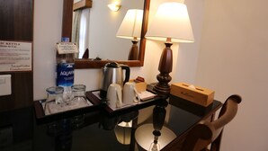Een hotelkamer met een tafel waarop een waterkoker, kopjes, een fles Aquafina water en zakdoekjes staan.