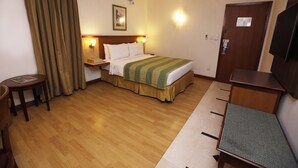 Een hotelkamer met een bed, een bureau, een stoel, een televisie en een airconditioning.