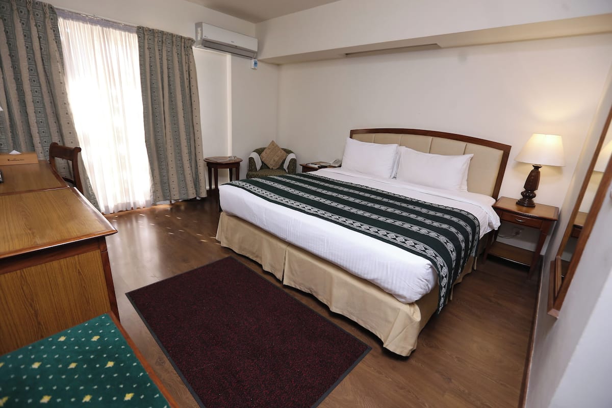 A hotel room with a bed, bedside table, lamp, chair, and a desk with a chair.