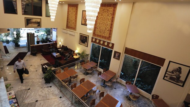Een hotel lobby met een marmeren vloer, meerdere zithoeken, grote ramen en decoratieve wandpanelen.
