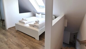 Une chambre à coucher moderne avec une lucarne, un plancher en bois et un lit blanc.