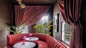 A cozy room with a curved red sofa, two small round tables, and a large window with curtains.