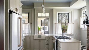 A kitchen with white cabinetry, a black and white checkered floor, a gas stove, and a window with curtains.