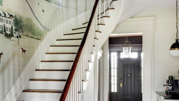 A staircase with a wooden handrail and white walls, leading to a dark door at the end.