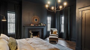 A bedroom with a large bed, a fireplace, a chandelier, and dark walls.