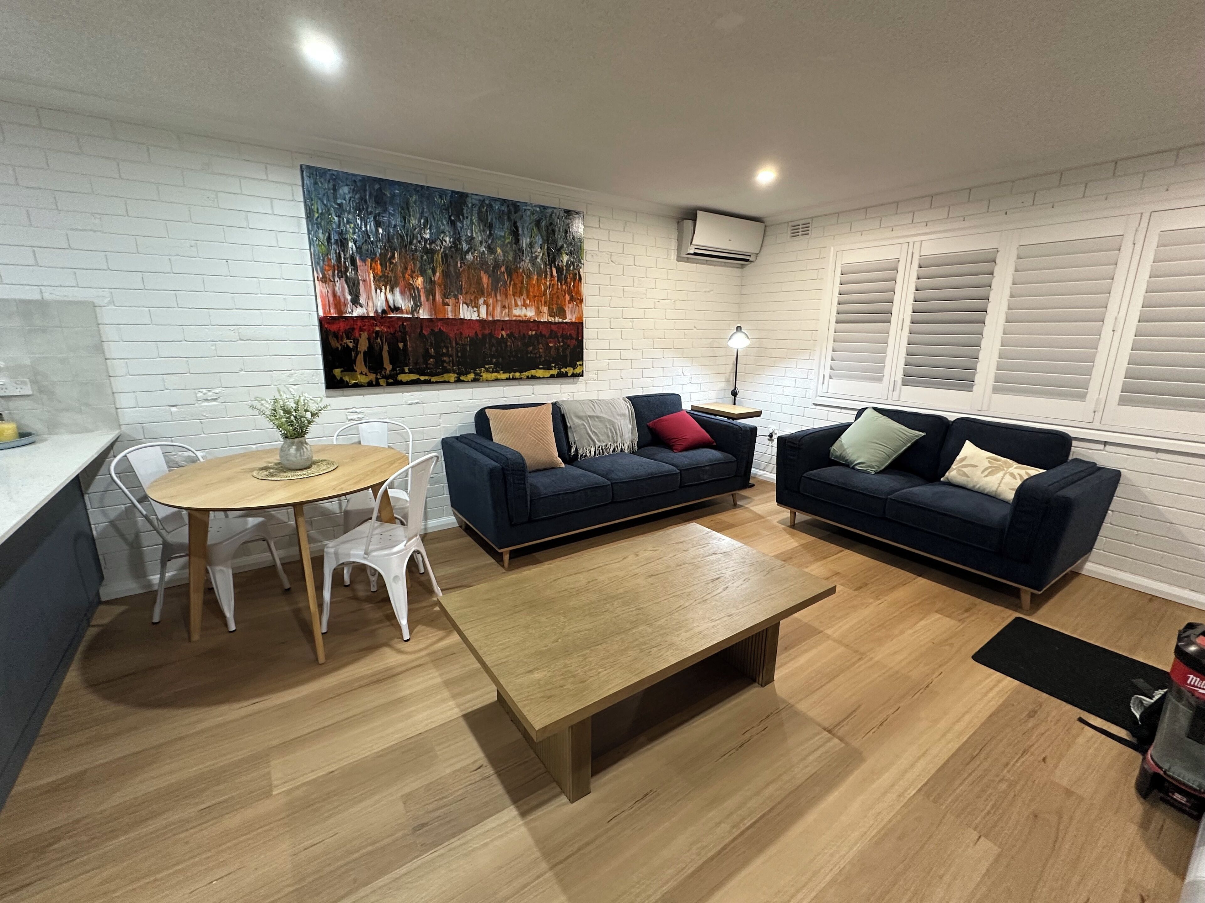 Una sala de estar moderna con dos sofás azul oscuro, una mesa de centro de madera, una mesa de comedor con sillas y un cuadro abstracto grande en la pared.