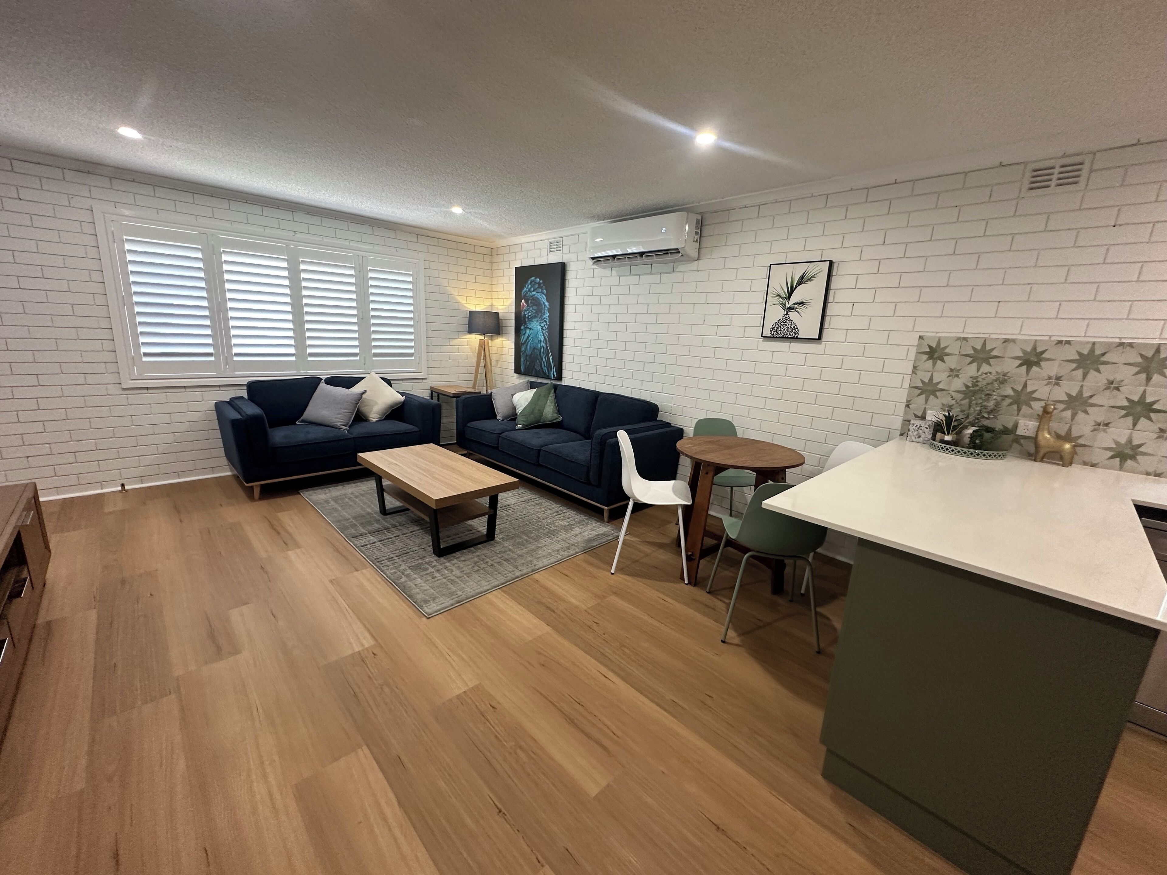A modern living room with a dark blue sofa, a wooden coffee table, and a small dining area with a white table and chairs.