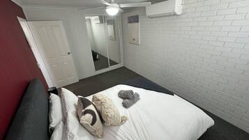 A hotel room with a bed, a ceiling fan, an air conditioning unit, a mirror, and a red wall.
