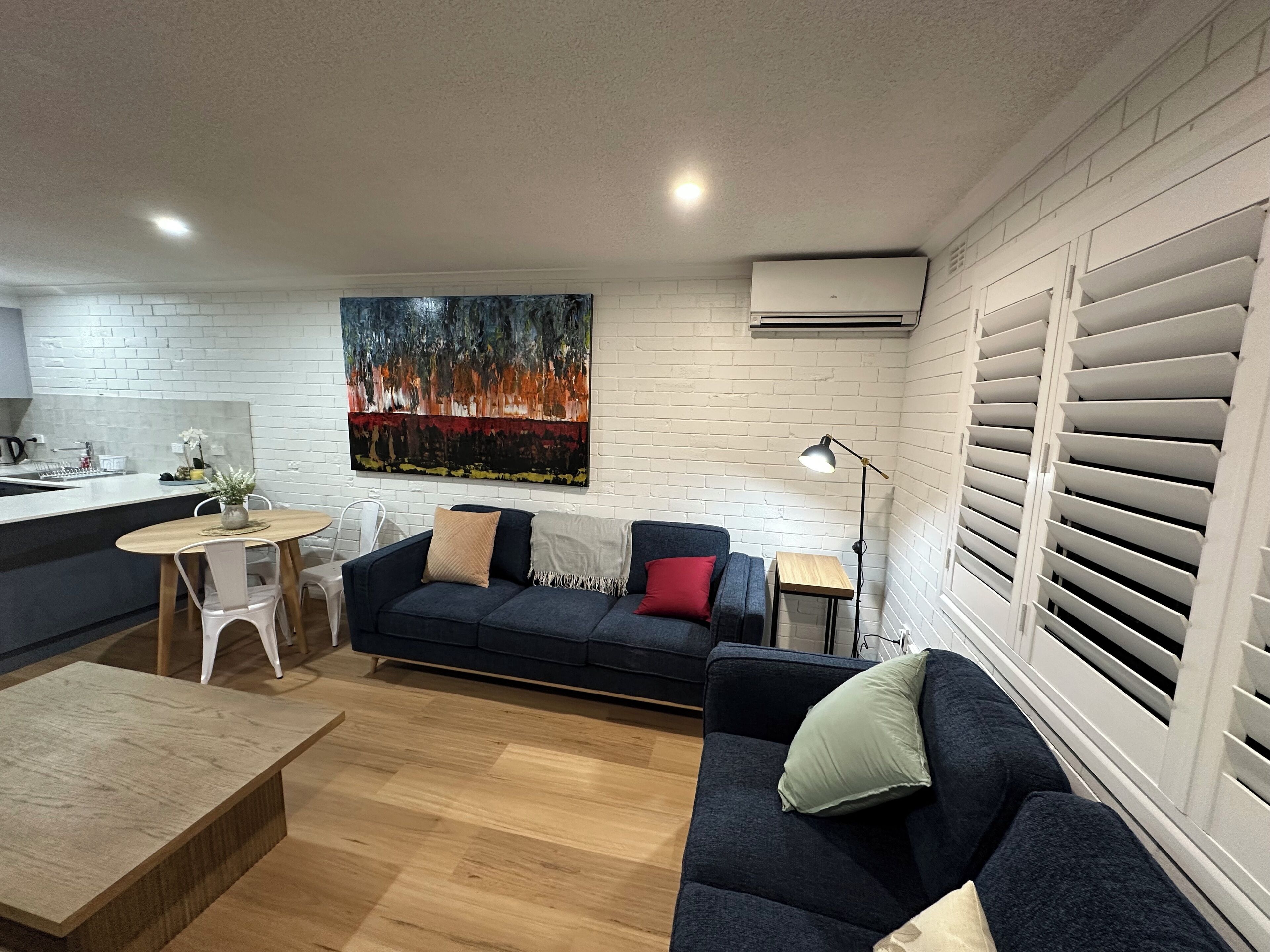 A modern living room with a dark blue sofa, a wooden coffee table, and a painting on the wall.