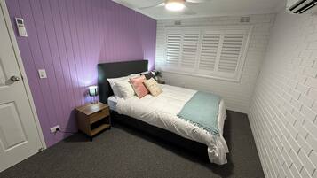 Ein Schlafzimmer mit Bett, Nachttisch, Deckenventilator und Fenster mit Rollläden.