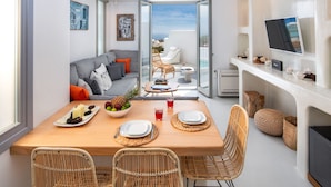 Ein modernes Wohnzimmer mit einem Holzespeisetisch, gedeckt für zwei Personen, einem grauen Sofa mit orangefarbenen Kissen, Korbstühlen und einem Balkon mit weißem Stuhl und Tisch.