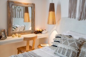 Un dormitorio con espejo de madera, mesita de noche con velas, lámpara colgante y cama con ropa de cama estampada.