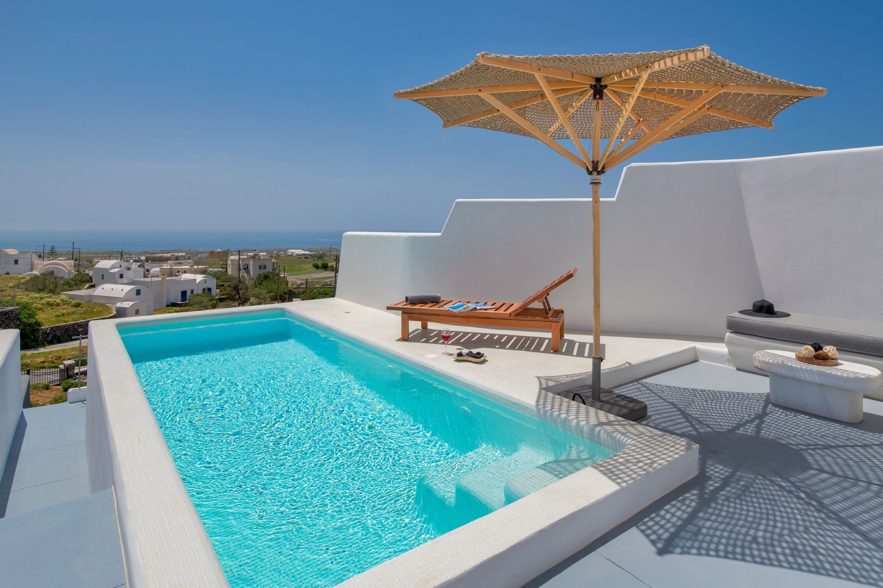 A rooftop pool with a clear view of the sea, a lounge chair, and a sun umbrella.