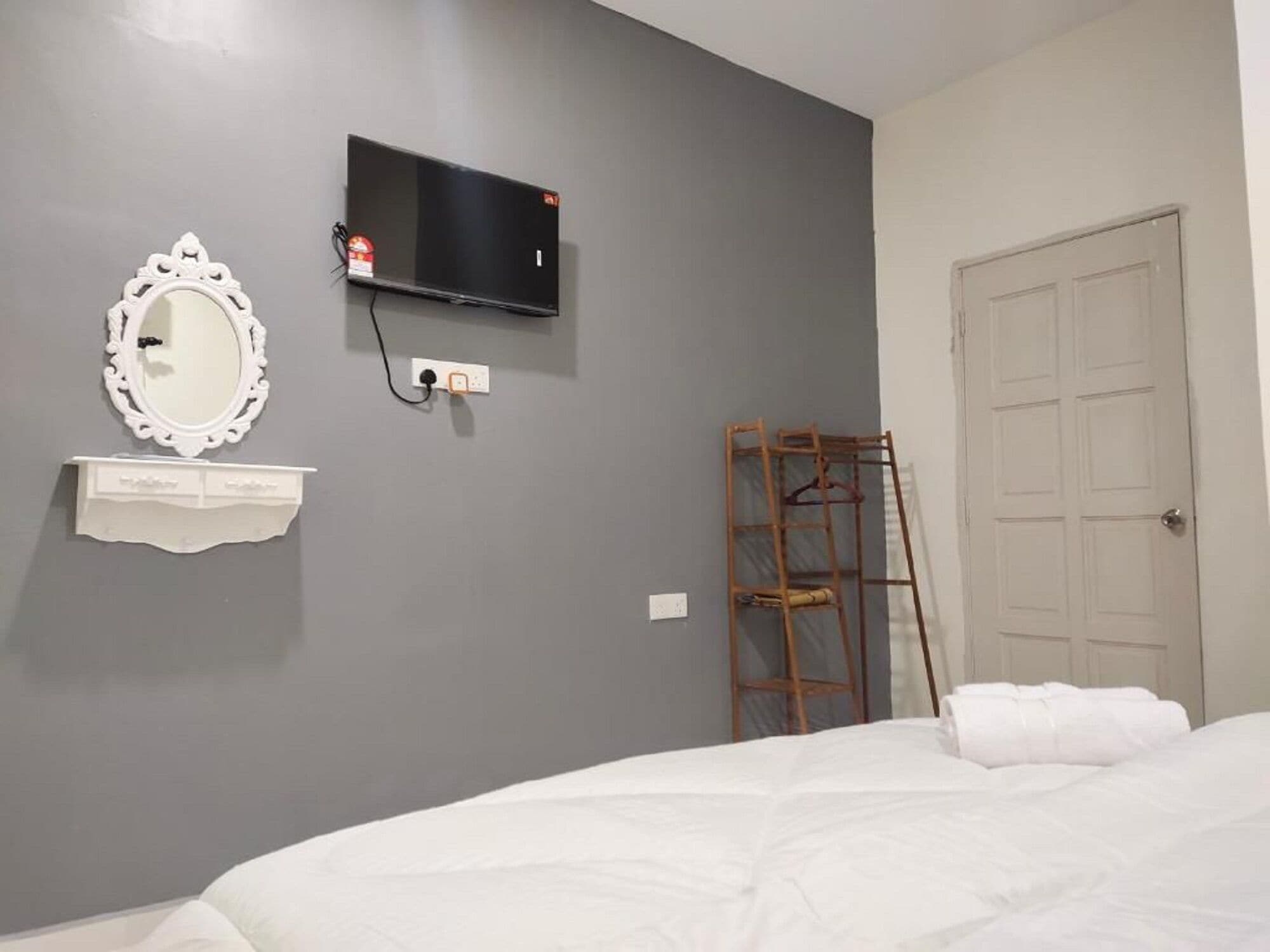 A bedroom with a bed, a white dresser, a mirror, a television, and a door.