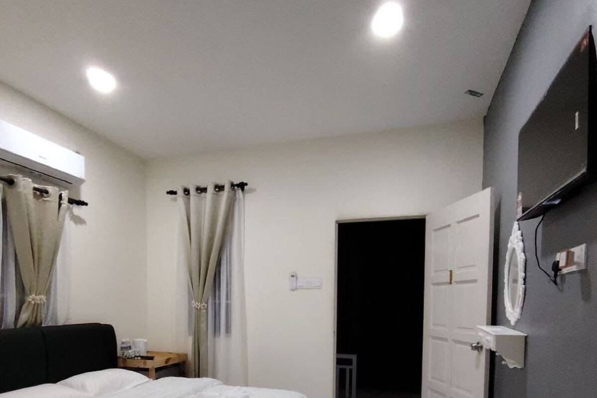 Un dormitorio moderno con una cama grande, una mesita de noche, un espejo y una puerta que da a un pasillo oscuro.