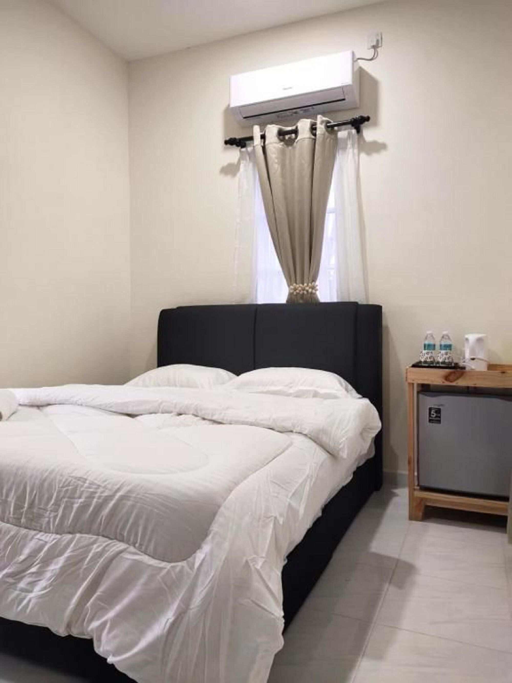 A bedroom with a bed, an air conditioning unit, a nightstand, and a small cabinet.