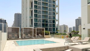 Area piscina sul tetto con sedie a sdraio e un piccolo angolo relax, circondata da edifici alti.