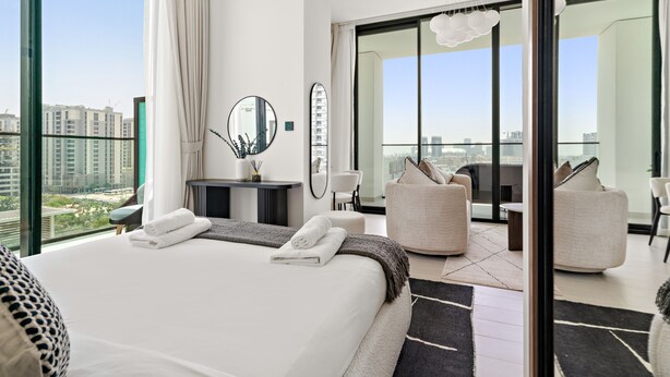 Una moderna camera d'hotel con un letto grande, un'area salotto con divano e poltrone, un tavolo da pranzo e vista sulla città attraverso ampie finestre.
