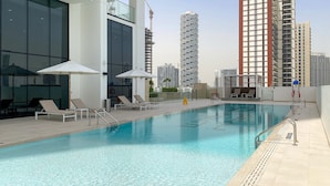 A rooftop pool with sun loungers and umbrellas, surrounded by modern buildings. - Binghatti Gardenia - 3305 1BD (Dubai)