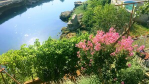 A river with rocky banks, lush greenery, and pink flowering bushes. - Charming 4-bedroom house with WiFi and AC in lovely Mostar (Mostar)