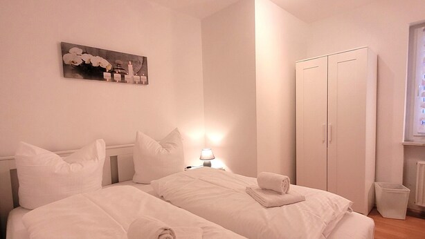 A hotel room with two beds, white linens, a bedside lamp, a painting on the wall, and a wardrobe. - Apartment in Winterberg Near Ski Lift (Winterberg)