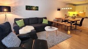 A modern living room with a sofa, a coffee table, and a dining area with a table and chairs. - Apartment in Winterberg Near Ski Lift (Winterberg)