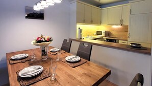 A dining area with a wooden table set for four, surrounded by chairs. A vase with flowers is on the table, and there is a microwave and stove in the adjacent kitchen area. - Apartment in Winterberg Near Ski Lift (Winterberg)