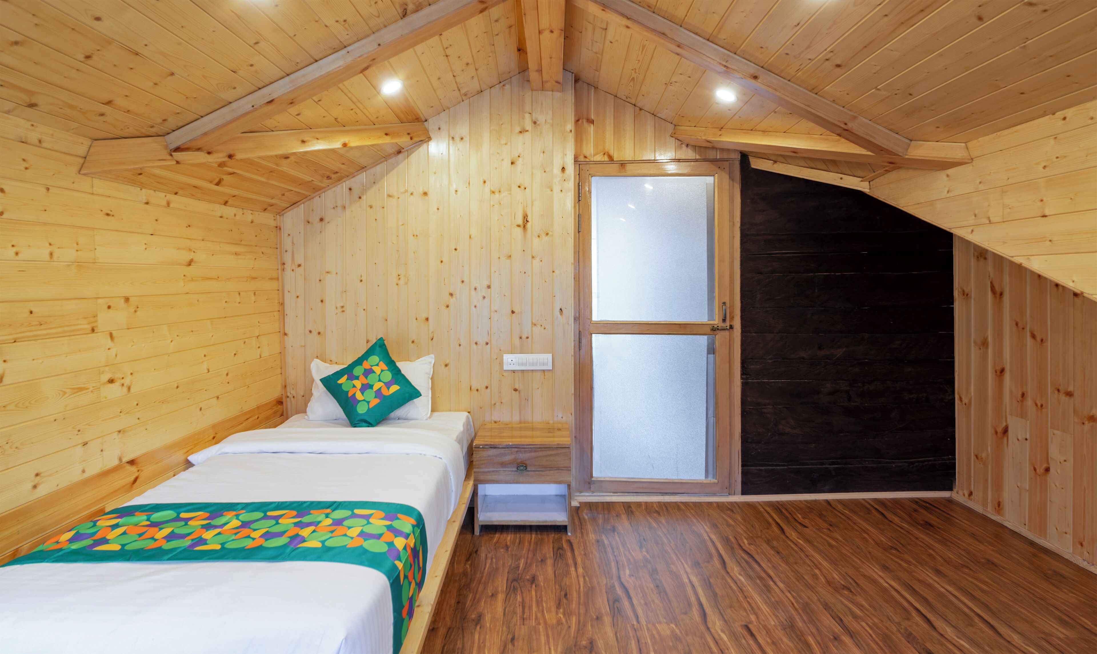A wooden room with a bed, a nightstand, a window, and a door.