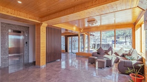 Un lobby amplio con techo de madera, suelo de mármol, un ascensor moderno y una zona de estar con vistas al exterior.