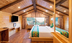 A wooden cabin bedroom with a bed, seating area, and a TV on the wall. - Treebo MR Villa with Mountain View (Manali)