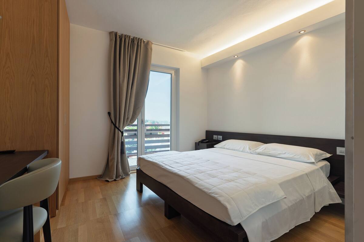 A modern hotel room with a bed, a desk, and a view of the outdoors.