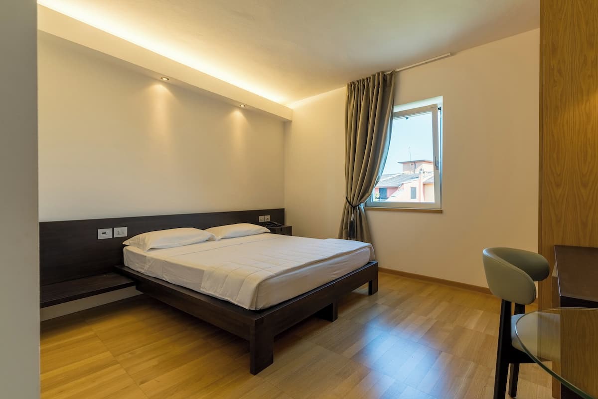 A bedroom with a bed, bedside table, and a window with curtains.