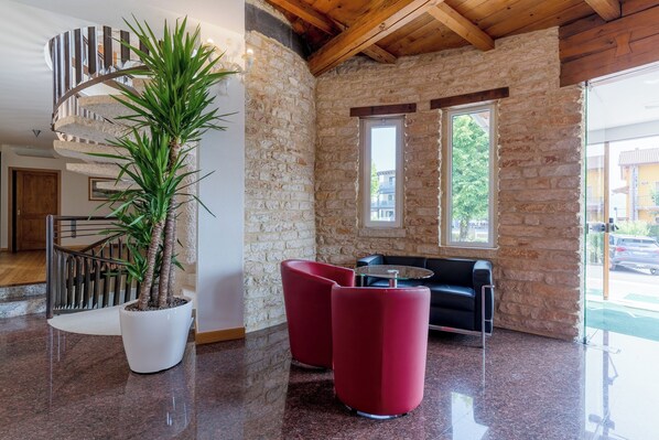 A modern interior with a spiral staircase, a potted plant, red chairs, and a black sofa.