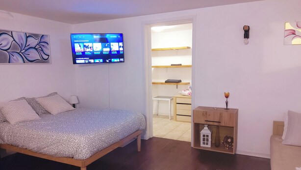 Ein Schlafzimmer mit einem Bett, einem an der Wand montierten Fernseher, einem Schreibtisch und einem Regal mit Dekorationen.