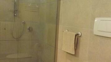 Een badkamer met een douchecabine van glas, twee toiletten, een wastafel en een toiletpapierhouder.