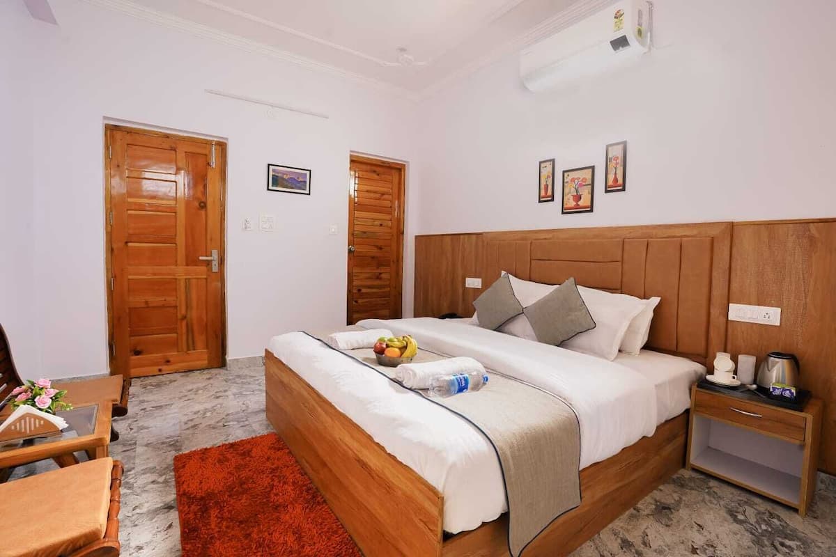 A hotel room with a wooden bed, a nightstand, a desk with a chair, and a red rug.