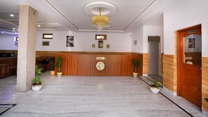 Een hotellobby met een receptiebalie, houten lambrisering, een kroonluchter en potplanten.