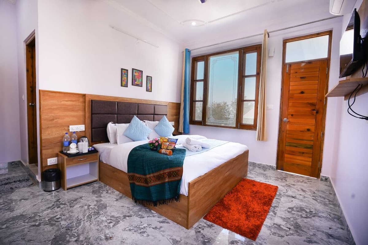 A hotel room with a bed, bedside table, window, and a door.